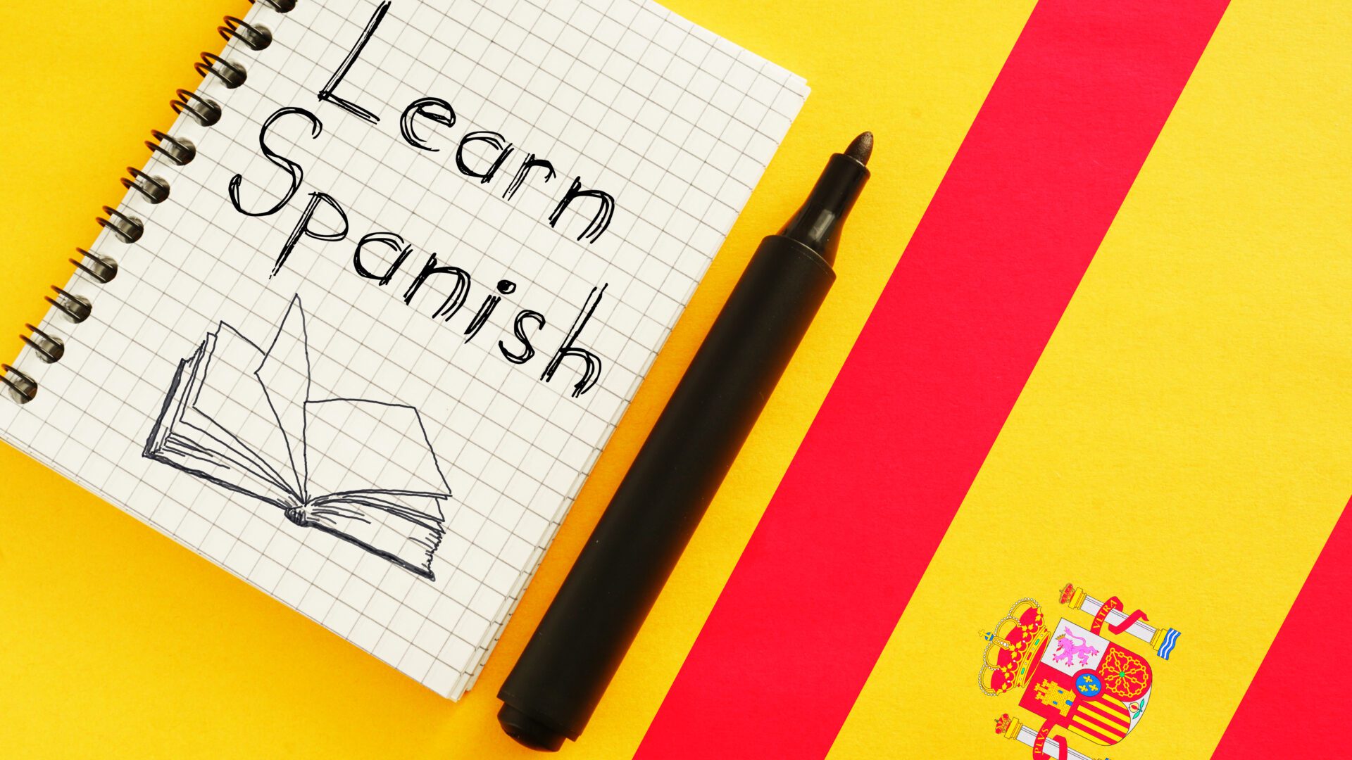 Notebook and marker on Spanish flag background.