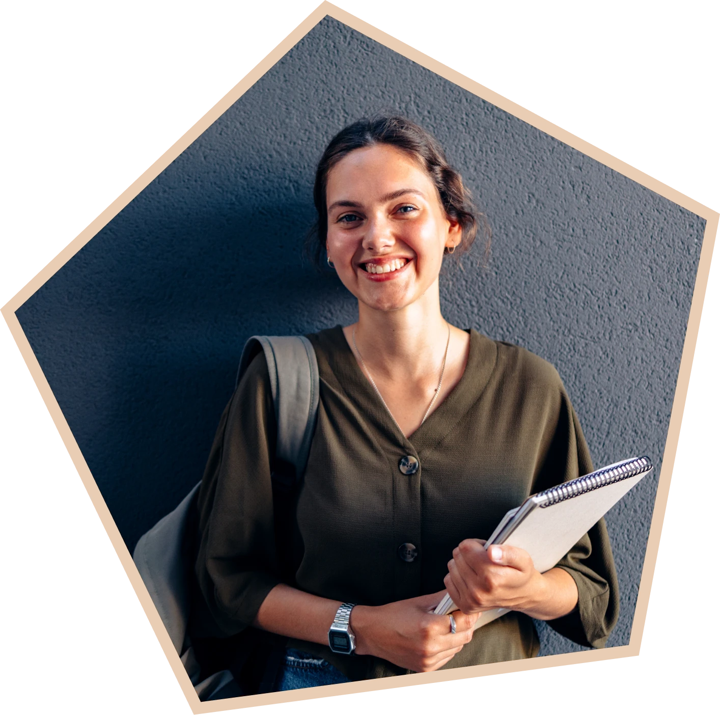 Smiling person holding notebooks against gray wall.
