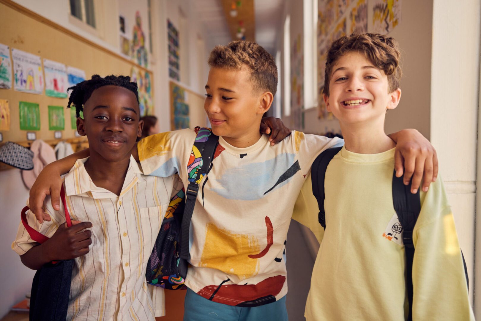 Elementary age students with backpacks embracing in school hallway, showcasing diversity and friendship